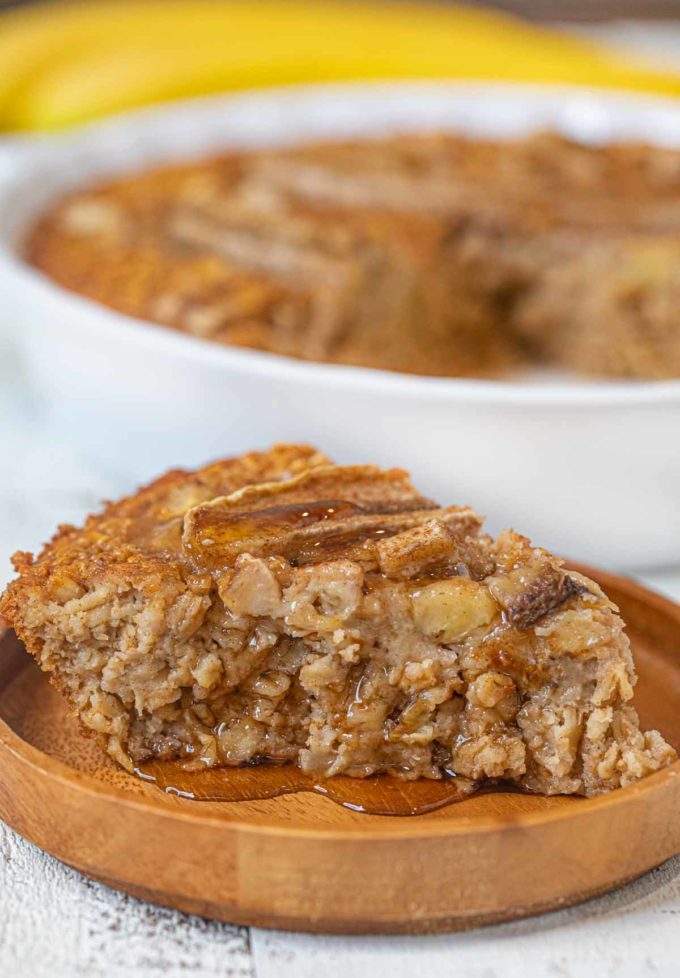 Slice of banana baked oatmeal on small wooden plate with maple syrup