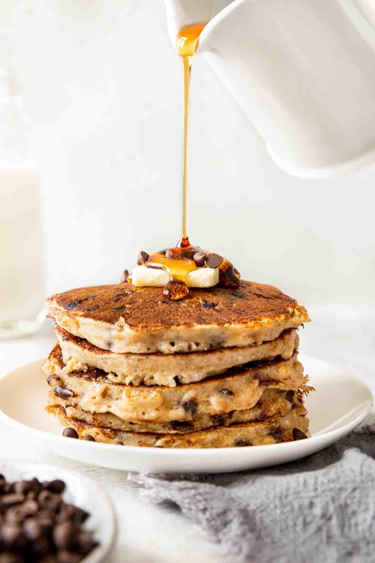 Whole Wheat Chocolate Chip Pancakes on a plate with butter and chips with syrup poured on top