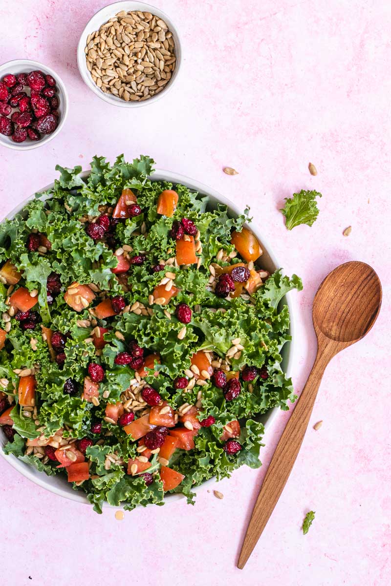 Kale Salad in a bowl with wooden spoon and additional ingredients 