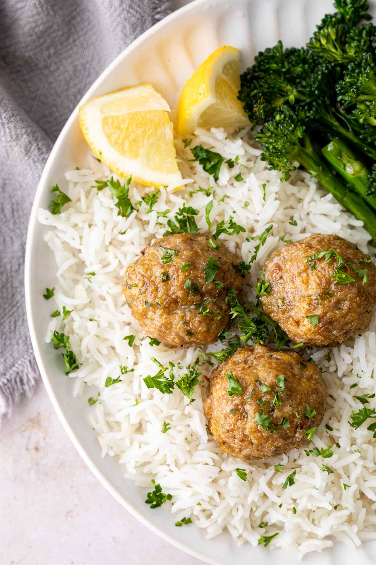 Turkey Meatballs on a plate with rice, broccolini and lemon wedges